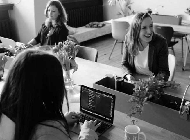 Three women at a table working with 
                laptops in front of them.